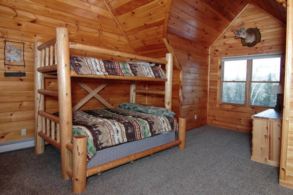A warm, family-friendly room with a sturdy bunk bed, wood-paneled walls, a window with a scenic view, and a nightstand. The space is designed for sharing stories, relaxing together, and enjoying the outdoors from the comfort of inside.
