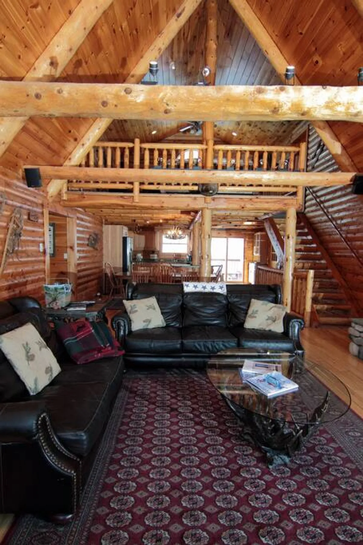 Inside, the great room boasts black leather sofas, wooden beams, and a welcoming area rug centered around a glass coffee table. The space radiates warmth and sociability, perfect for group gatherings after a day outside. The setup invites guests to gather for cocoa, share stories by the fireplace, or relax together in comfort.
