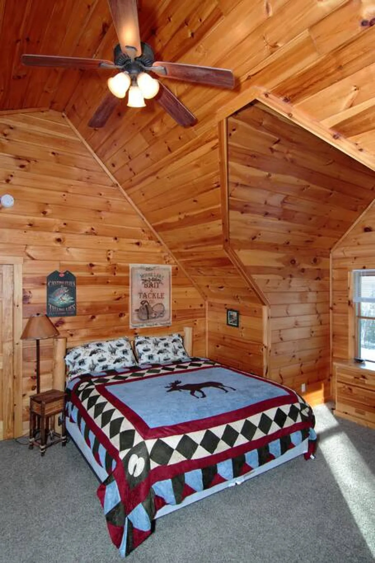 A spacious bedroom with a wooden ceiling, quilted king-size bed, decorative wall accents, nightstands, and a soft lampshade. Natural light streams through the windows, creating a cozy and inviting ambiance perfect for relaxation and privacy.