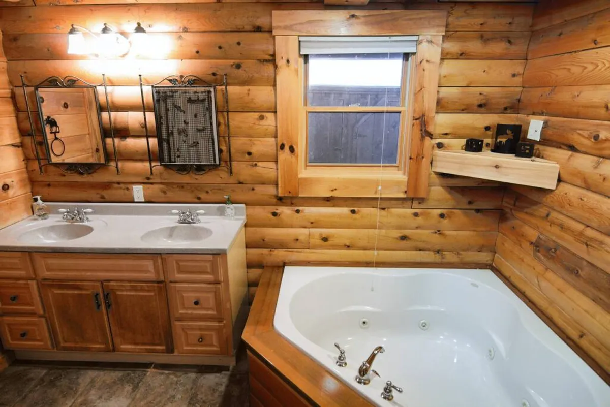 A luxurious en-suite bathroom featuring a jacuzzi tub, double sink vanity, wood-paneled walls, and large mirrors. The setting exudes tranquility and spa-like indulgence, perfect for unwinding after a day of mountain adventures.