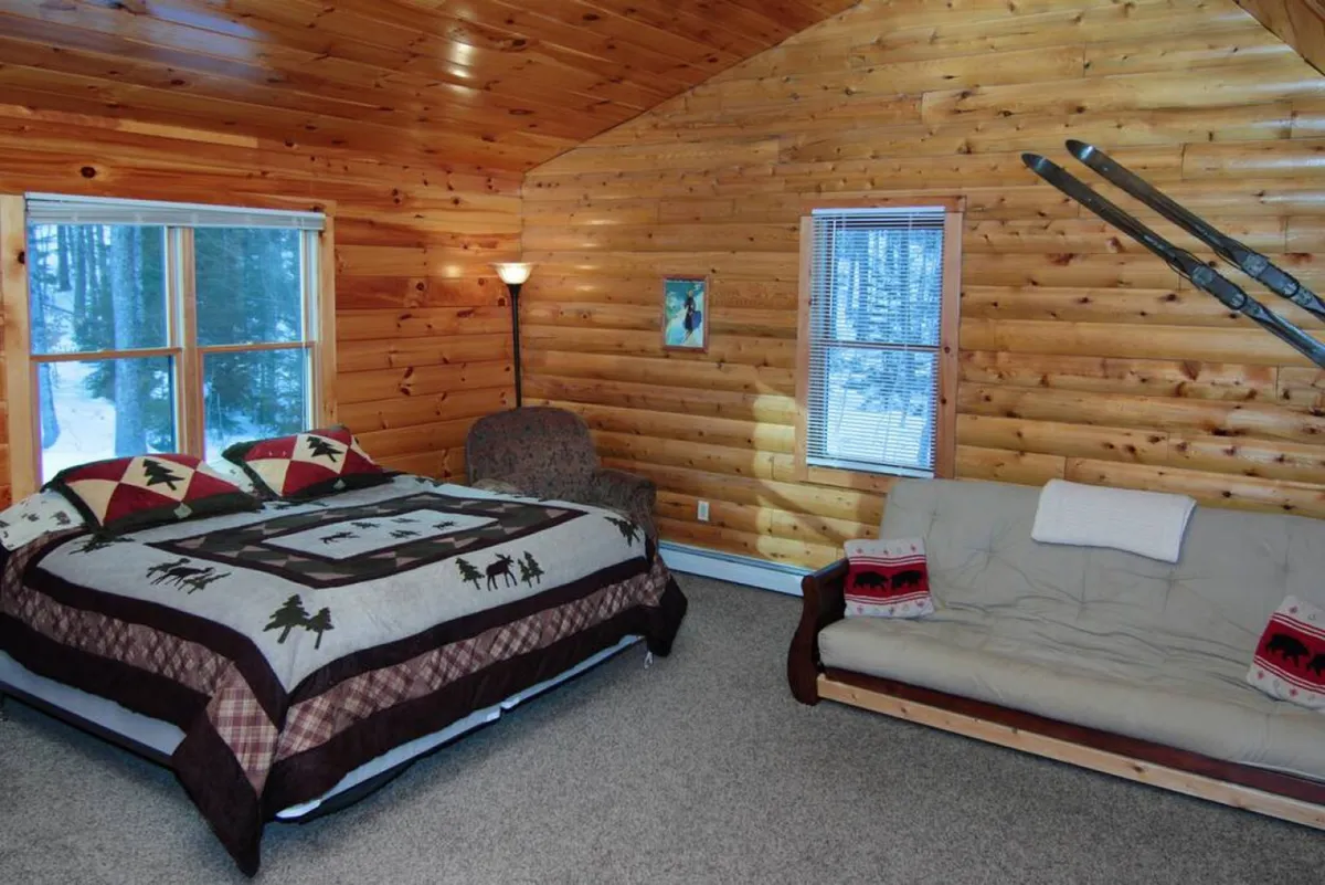 A king suite with a patterned duvet on the bed, a cozy sitting area with a sofa, wood-paneled walls, and expansive windows offering beautiful outdoor views. The space feels both intimate and spacious, ideal for unwinding alone or sharing with a loved one.